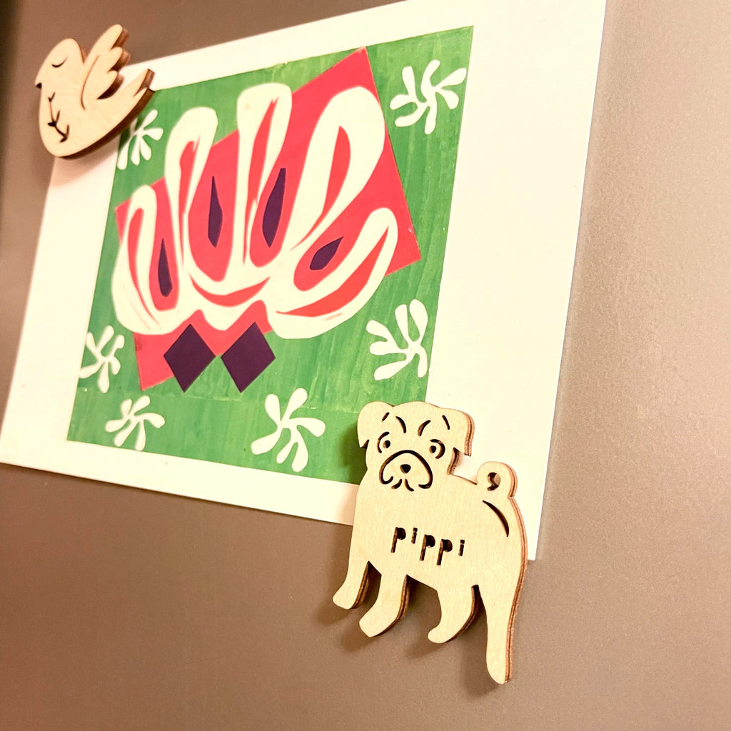Image of wooden pug ornament on fridge holding a 4"x6" postcard