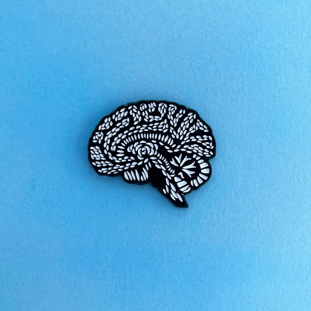 black and white metal enamel pin on a light blue background
